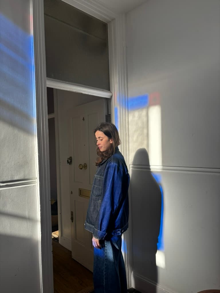 Ana Dunne Sequi in profile in a doorway, eyes lowered, her shadow on the wall beside her